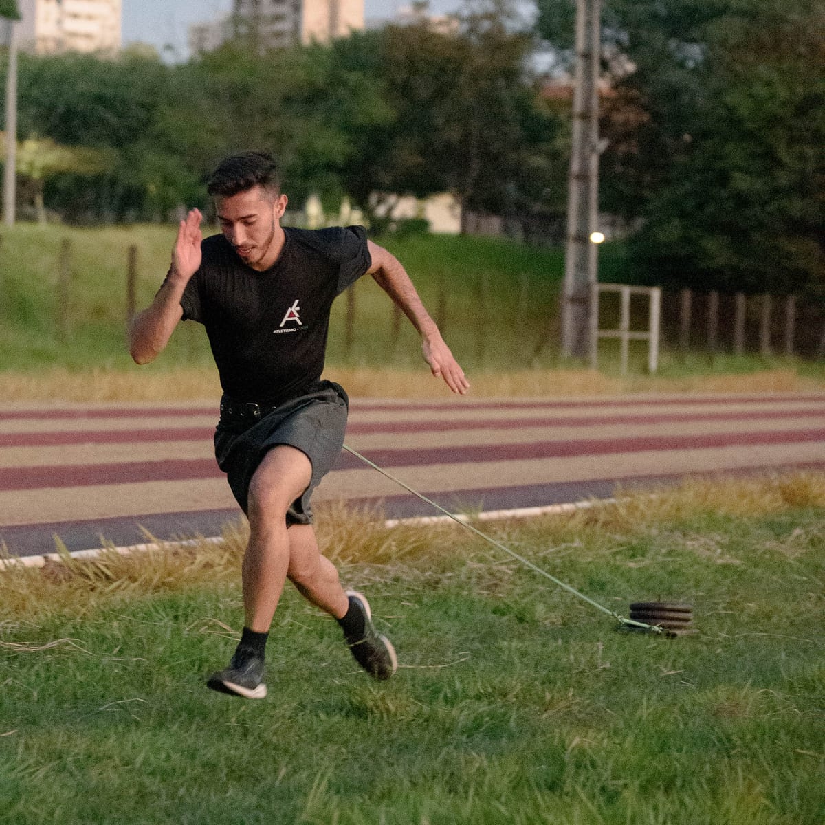 Atleta com camiseta do Atletismo UEM realiza exercício de arrasto de trenó na pista durante treino de preparação para o JOIA