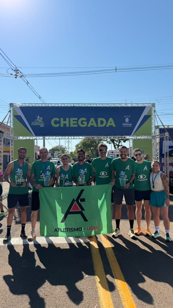 Integrantes da equipe Atletismo UEM posam com troféus e a bandeira do projeto sob o pórtico de chegada da Prova Rústica de Floriano